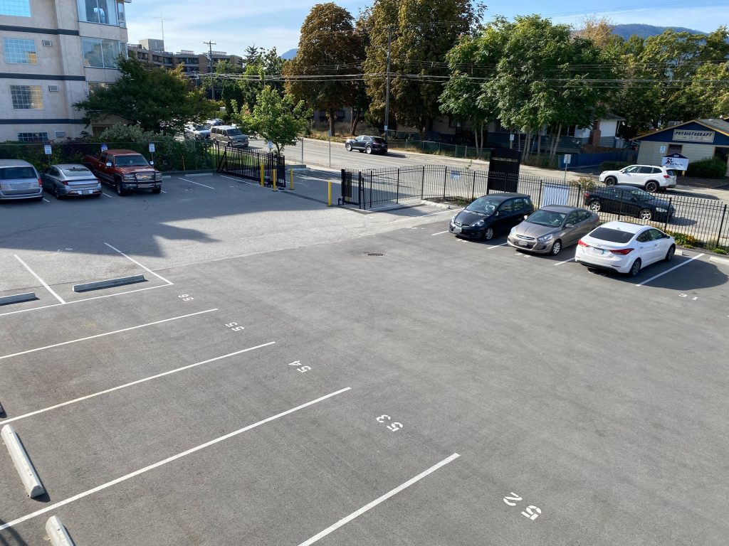 Parking lot in 352 Urban Centre. There are a few cars in the background, trees, and other ubuildings. 